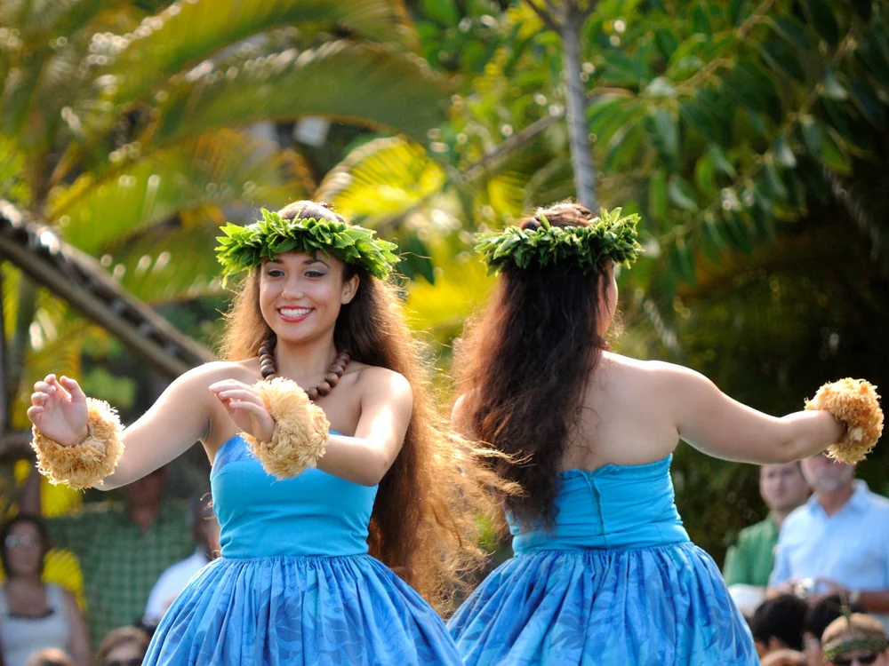 Hula dancers in blue dresses performing on the lagoon during the Huki canoe pageant at the Polynesian Cultural Center's Hawaiʻi village