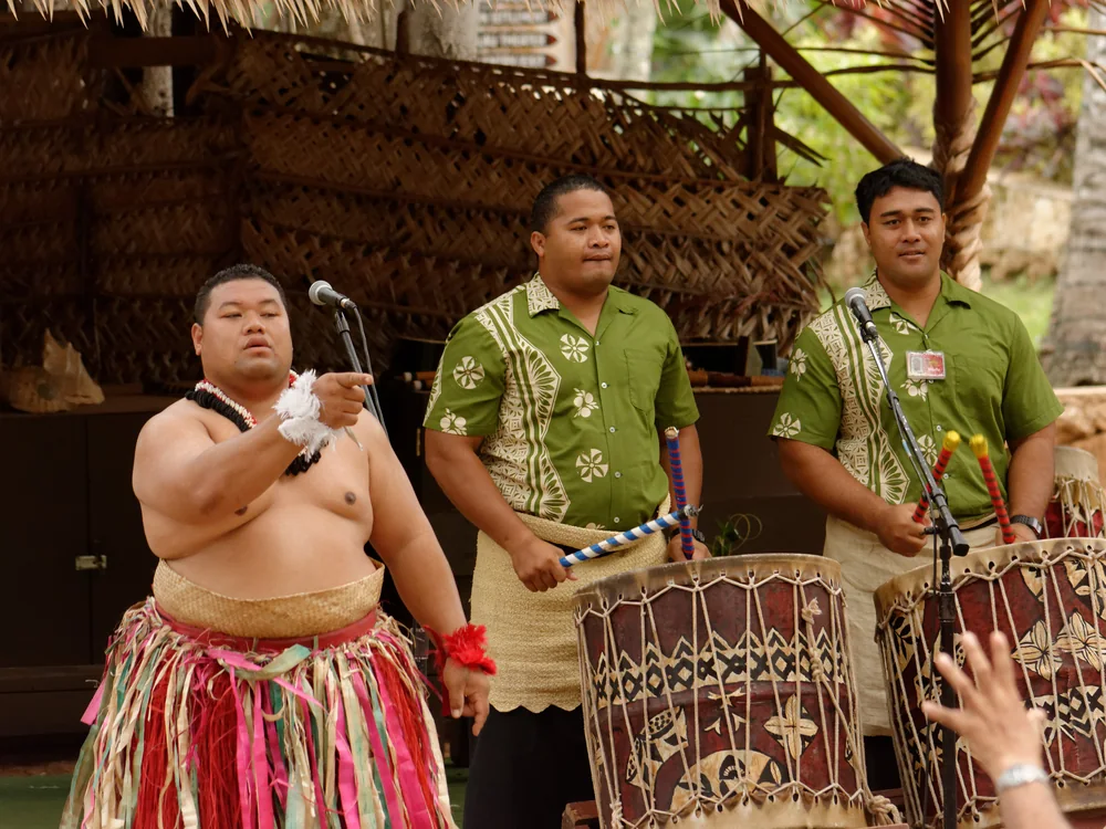 Three performers in traditional dress playing lali log drums at the Polynesian Cultural Center's Tonga village